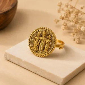 Gold-tone traditional statement ring featuring an intricate circular relief design of three devotional figures, surrounded by beaded detailing, displayed on a cream-colored stone jewelry stand.