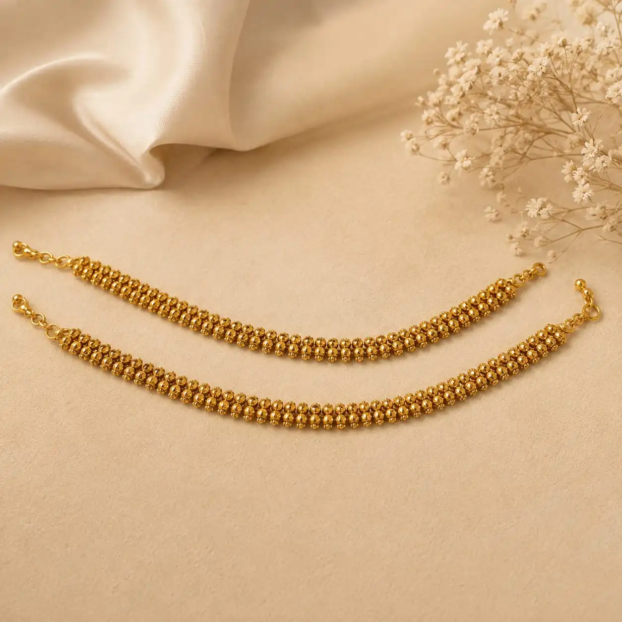 Gold-tone beaded double-layer jewelry chain displayed on a soft cream background with floral accents