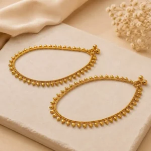 Golden Bead Grace Payal featuring delicate gold-tone chain detailing and evenly spaced teardrop-shaped bead accents, displayed on a cream stone surface with soft beige fabric and dried flowers.