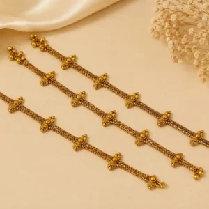 Royal Floral Beaded Gold Tone Payal featuring delicate chainwork, repeated floral motifs and small ornamental bead details, displayed on a soft beige background with satin fabric and dried flowers.
