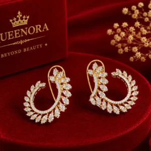 Gold-tone floral hoop earrings with sparkling leaf-shaped stone details displayed on a red velvet pedestal with luxury Queenora packaging and decorative accents.