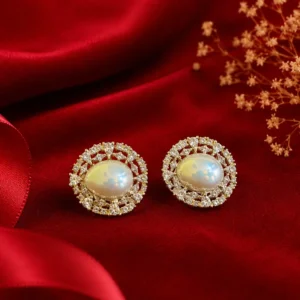 Pearl halo stud earrings with luminous oval centers and sparkling stone detailing displayed on rich red velvet with elegant jewelry box accents.