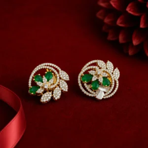A pair of elegant gold-tone stud earrings with emerald-green gemstone accents and sparkling crystal leaves are displayed on a rich red velvet surface. The intricate floral-inspired design is highlighted by soft studio lighting, creating a luxurious and sophisticated jewelry presentation. A satin red ribbon appears in the foreground, while a blurred red flower in the background adds depth and elegance to the composition.