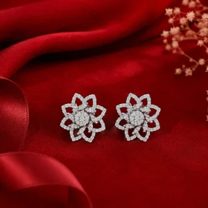 Elegant silver floral stud earrings with sparkling stones displayed on luxurious red fabric.