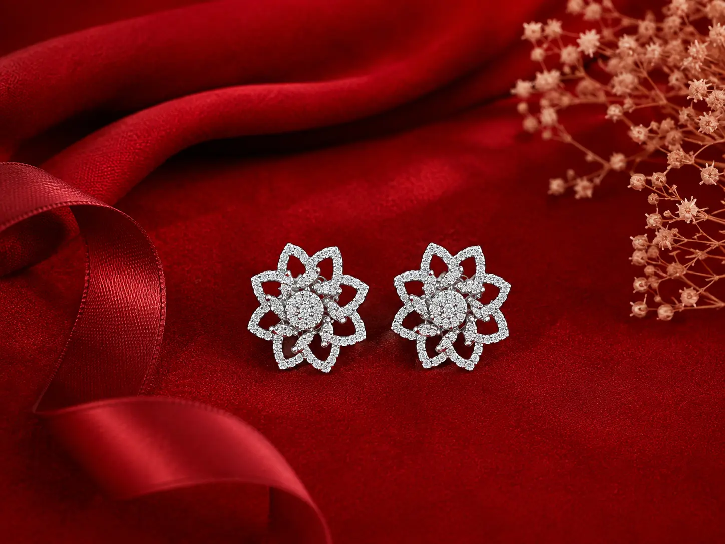 Elegant silver floral stud earrings with sparkling stones displayed on luxurious red fabric.