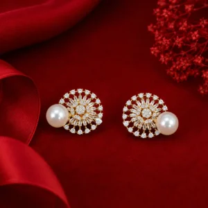 Elegant gold-toned stud earrings featuring a circular sunburst design with sparkling clear stones and large white pearl accents, displayed on rich red velvet fabric with red floral elements in the background.