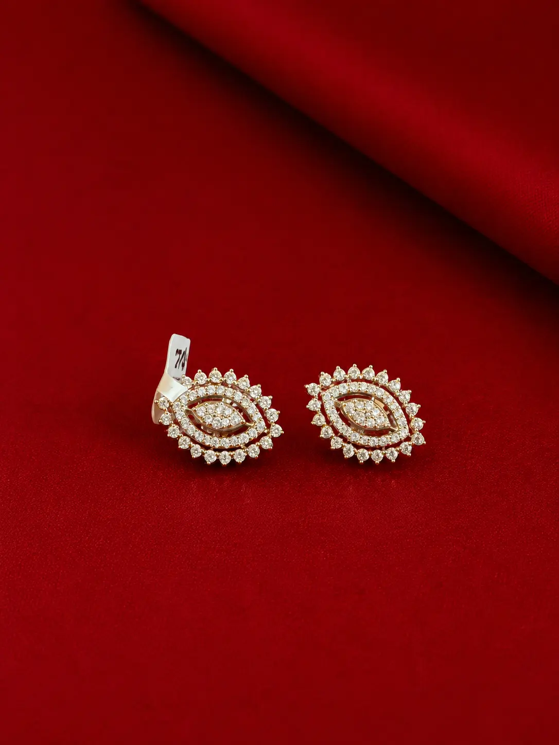 Gold-tone floral stud earrings with sparkling clear stones displayed on a luxurious red background.