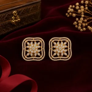 Gold floral stud earrings with sparkling stone detailing, displayed on rich burgundy velvet with an elegant jewelry box and decorative dried flowers.