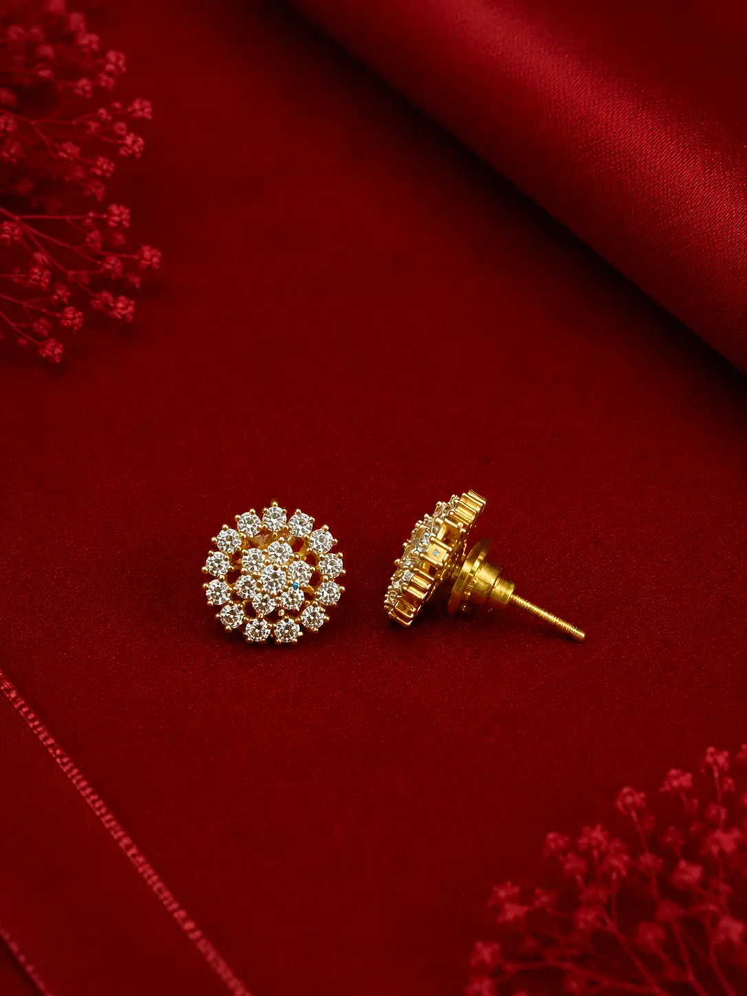 Elegant gold-tone floral crystal stud earrings displayed on a rich red satin background with delicate decorative accents