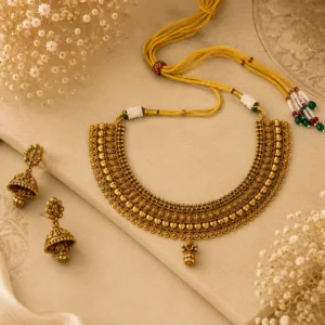 Queenora traditional antique gold-tone necklace and matching jhumka earrings displayed inside a luxurious deep-red velvet jewelry box with “Queenora – Beyond Beauty” branding and a soft beige-gold background.