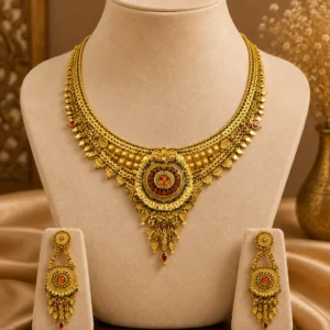 Gold-tone traditional necklace set displayed on a cream jewellery mannequin with matching long drop earrings, intricate layered detailing, ornate central pendant and red gemstone accents on a warm beige background.