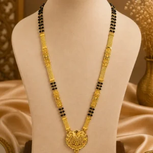 Gold-tone traditional black bead necklace displayed on a cream jewellery mannequin, featuring intricate ornamental detailing, a large decorative central pendant and elegant layered chainwork against a warm beige background.