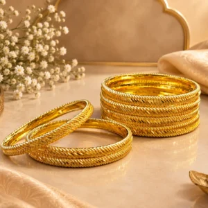 Gold-tone traditional bangles with intricate braided and beaded detailing displayed on a luxurious beige surface with silk fabric and floral accents.