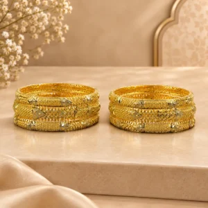 Six gold-tone traditional bangles arranged in two sets of three on a luxurious beige display surface, featuring intricate geometric lattice patterns, engraved detailing, textured borders, and decorative two-tone accents.