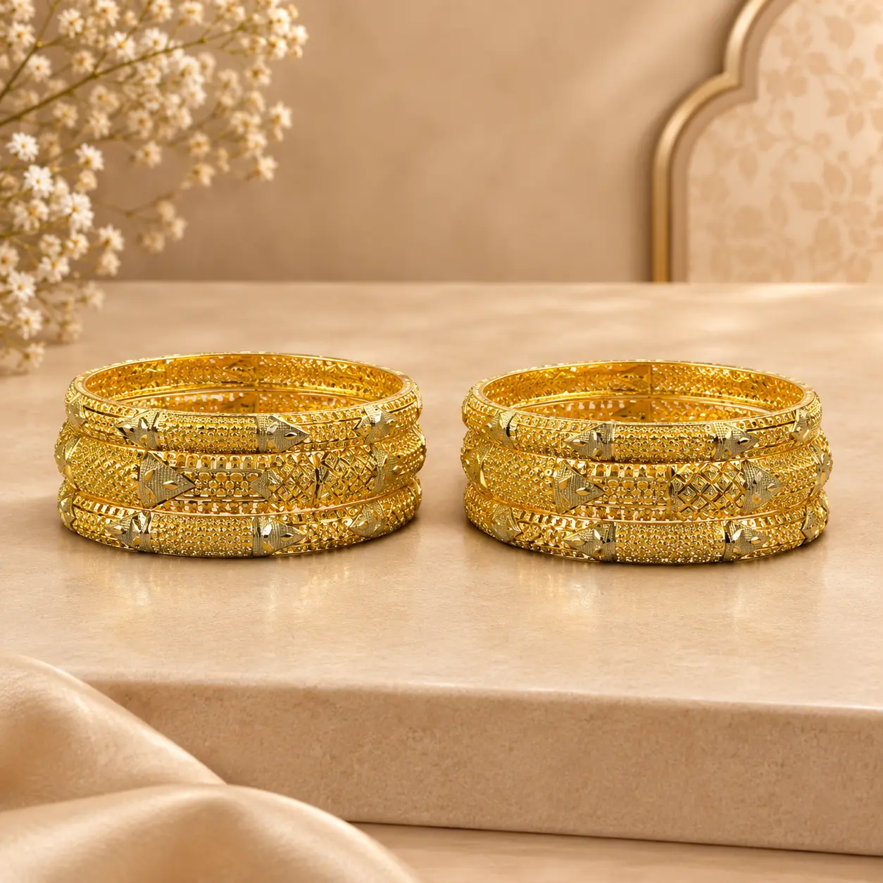 Six gold-tone traditional bangles arranged in two sets of three on a luxurious beige display surface, featuring intricate geometric lattice patterns, engraved detailing, textured borders, and decorative two-tone accents.