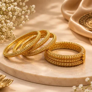 "Gold-tone designer bangles with intricate floral and geometric detailing displayed on a luxury jewellery background"